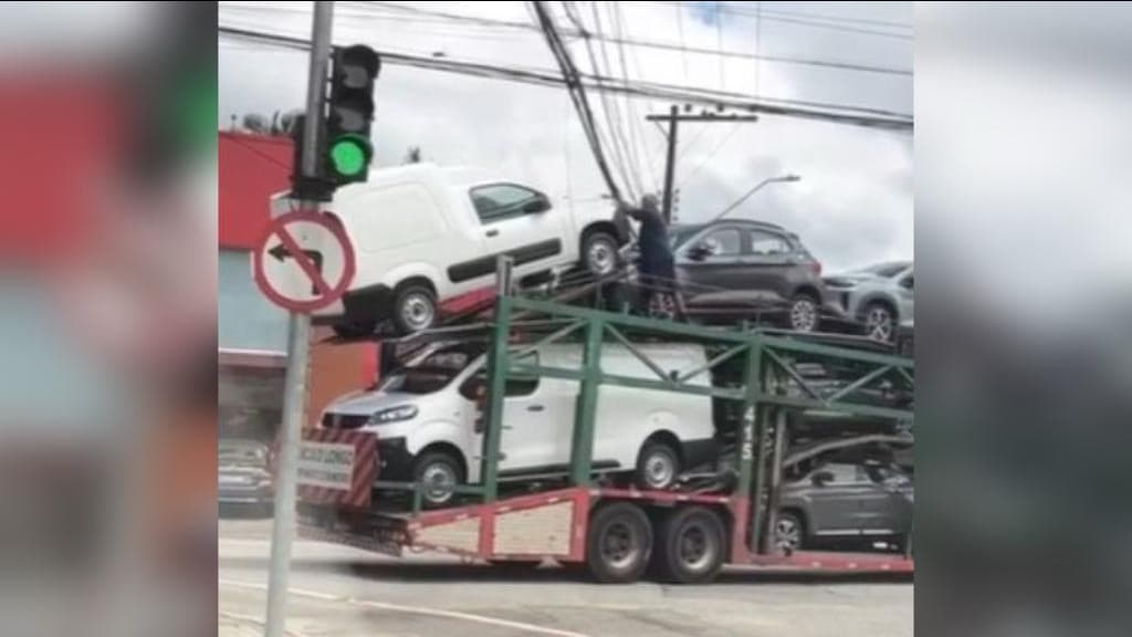 Homem levanta fios de rede elétrica para caminhão-cegonha passar