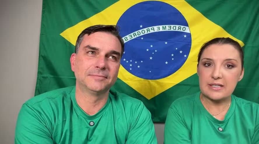 Flávio Bolsonaro e a economista Daniella Marques em gravação de vídeo diante de uma bandeira do Brasil