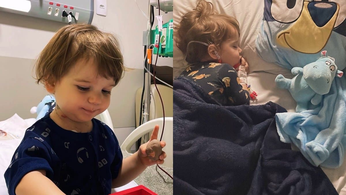 Bebê sentado na cama de hospital ao lado de equipamento de infusão e, ao lado, dormindo abraçado a um bichinho de pelúcia