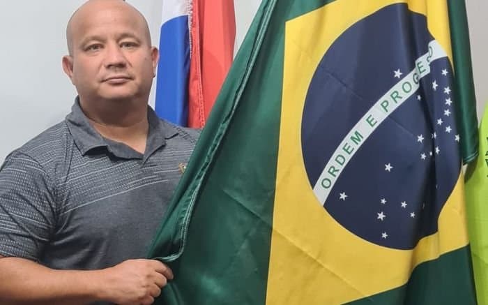 Homem de camisa polo cinza segurando a bandeira do Brasil