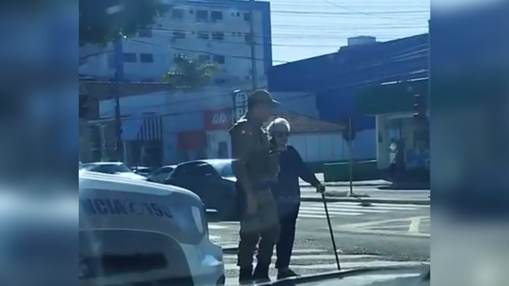 Policial militar para viatura no sinal verde e ajuda idosa a atravessar rua