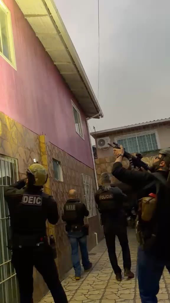 Policiais civis da DEIC armados em frente a uma casa durante a Operação Mosaico
