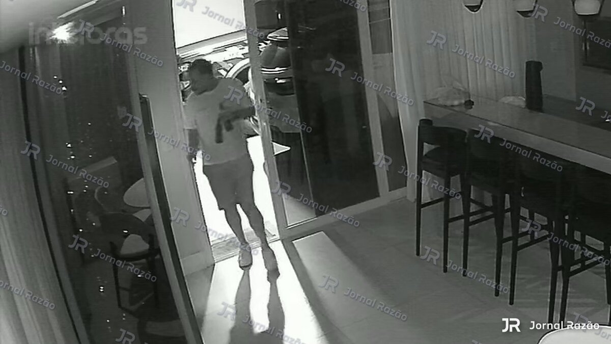 Fábio aparece na entrada da casa com duas garrafas nas mãos.